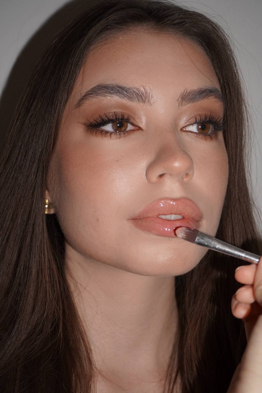 Liuba applying lip gloss on a client with soft, radiant makeup